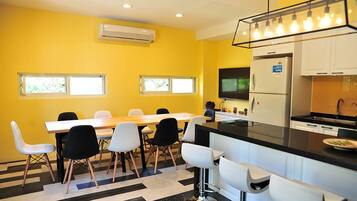 Una cocina moderna con encimera negra, armarios blancos y un refrigerador de acero inoxidable. Cuenta con un comedor con mesa y sillas de madera, y una zona de bar con taburetes.