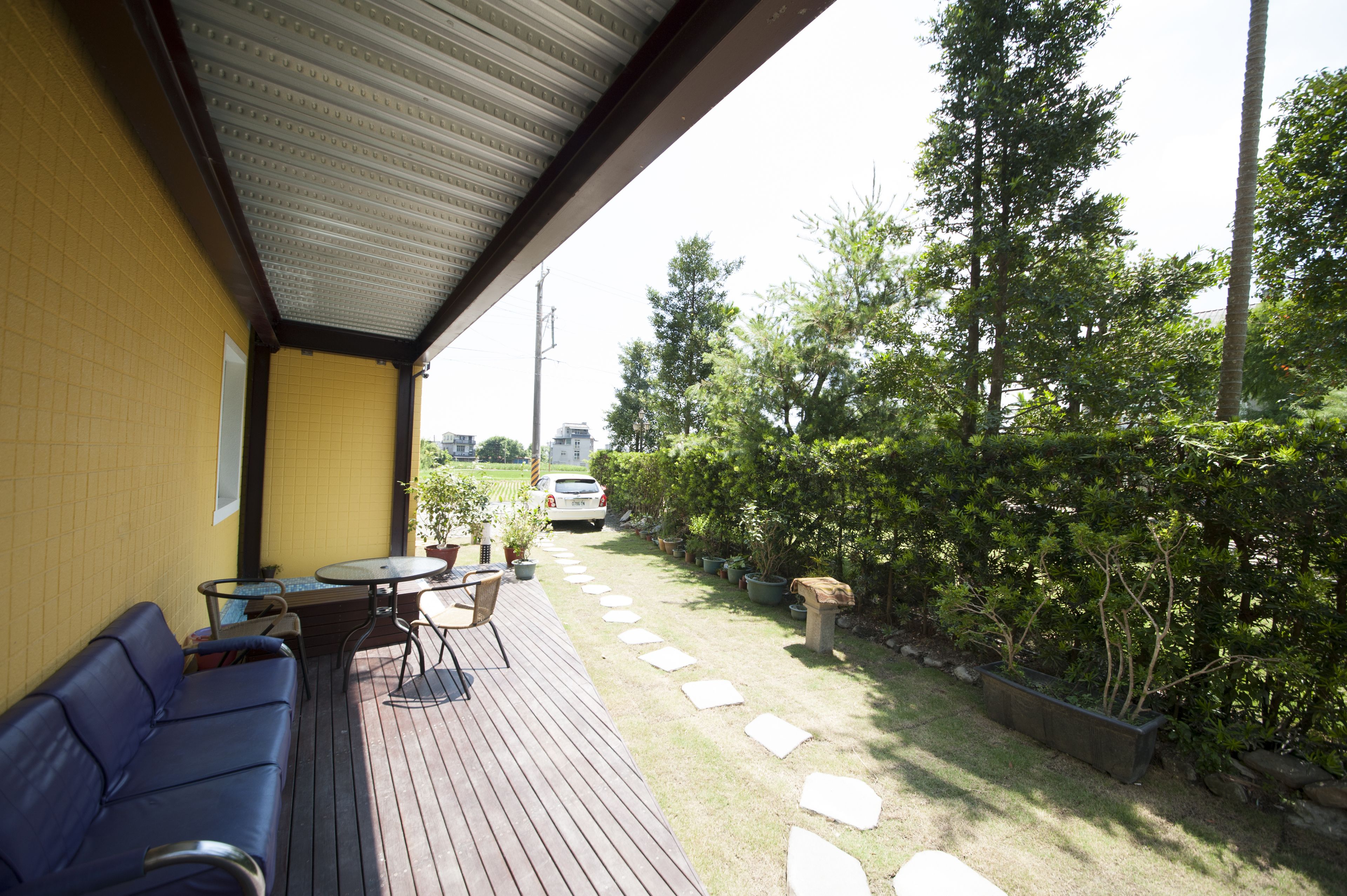 A covered outdoor seating area with a wooden deck, a blue sofa, and a small table with chairs.