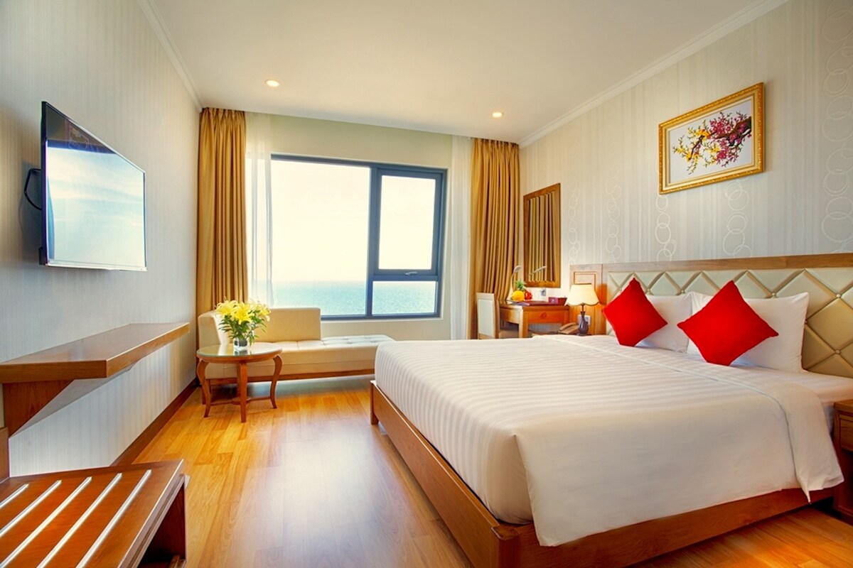 A hotel room with a bed, a desk, a chair, a TV, and a window with curtains.