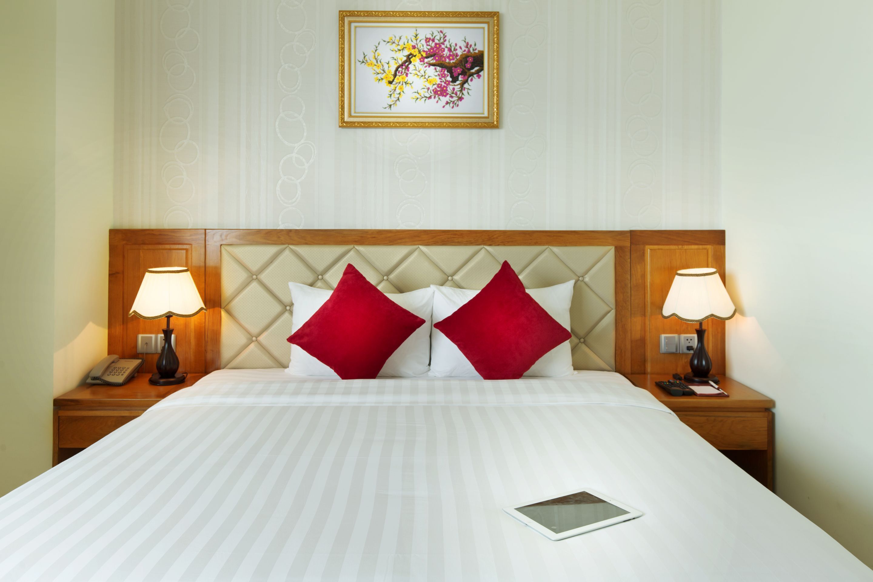A hotel room with a large bed, two bedside lamps, a telephone, and a framed artwork on the wall.