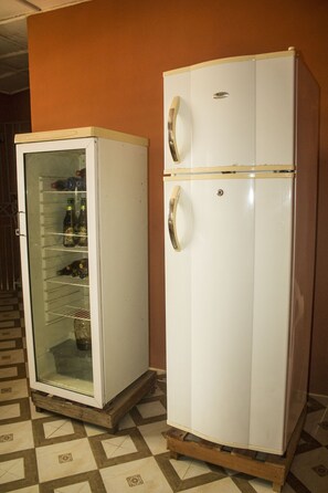 Un refrigerador blanco con puerta de vidrio y compartimento congelador, sobre un piso de baldosas con diseño geométrico.
