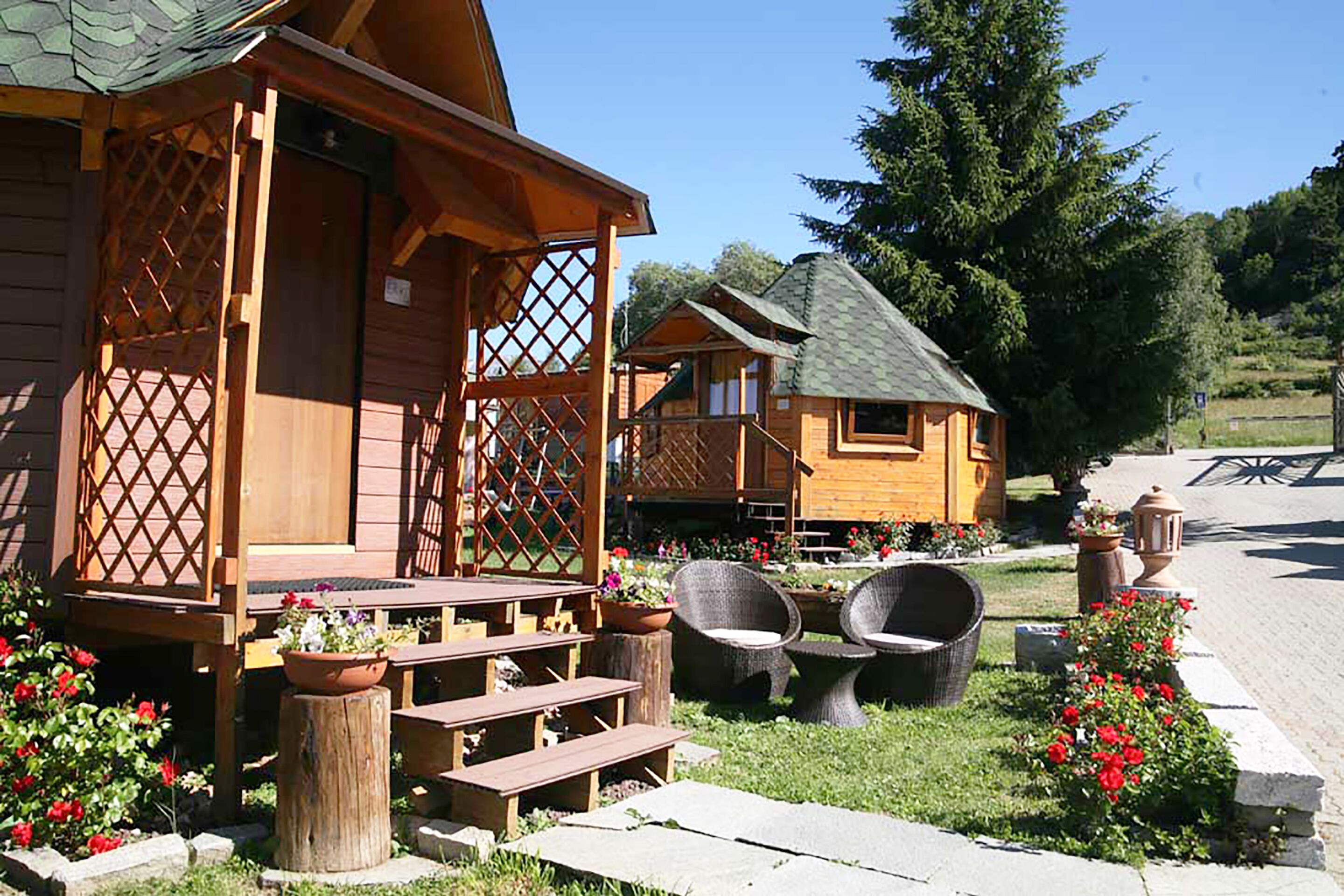 A wooden cabin with a porch, outdoor seating, and flower beds.