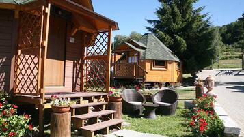 A wooden cabin with a porch, outdoor seating, and flower beds.