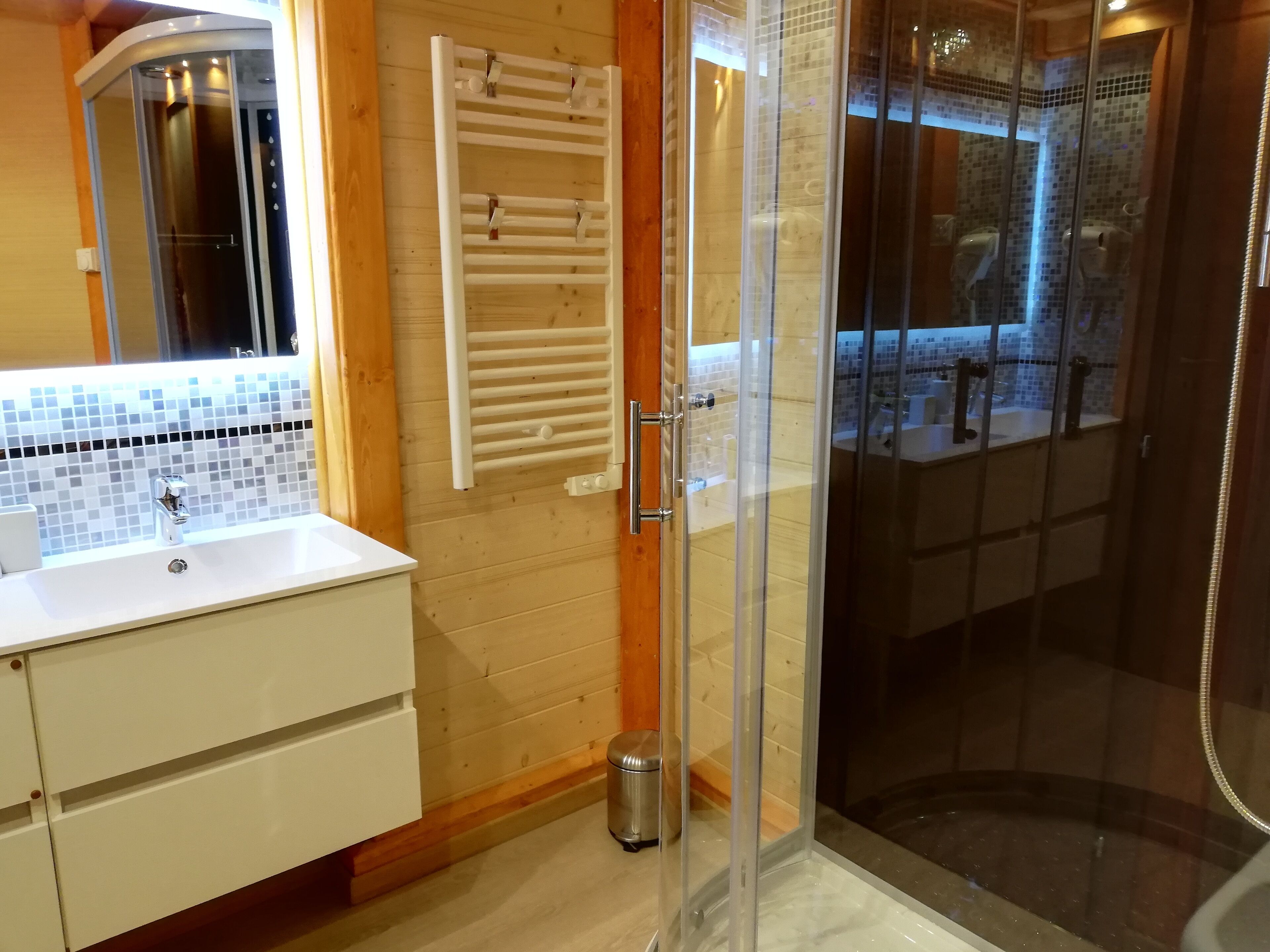 Un baño moderno con ducha de vidrio, lavamanos blanco con grifo cromado y tocador de madera.