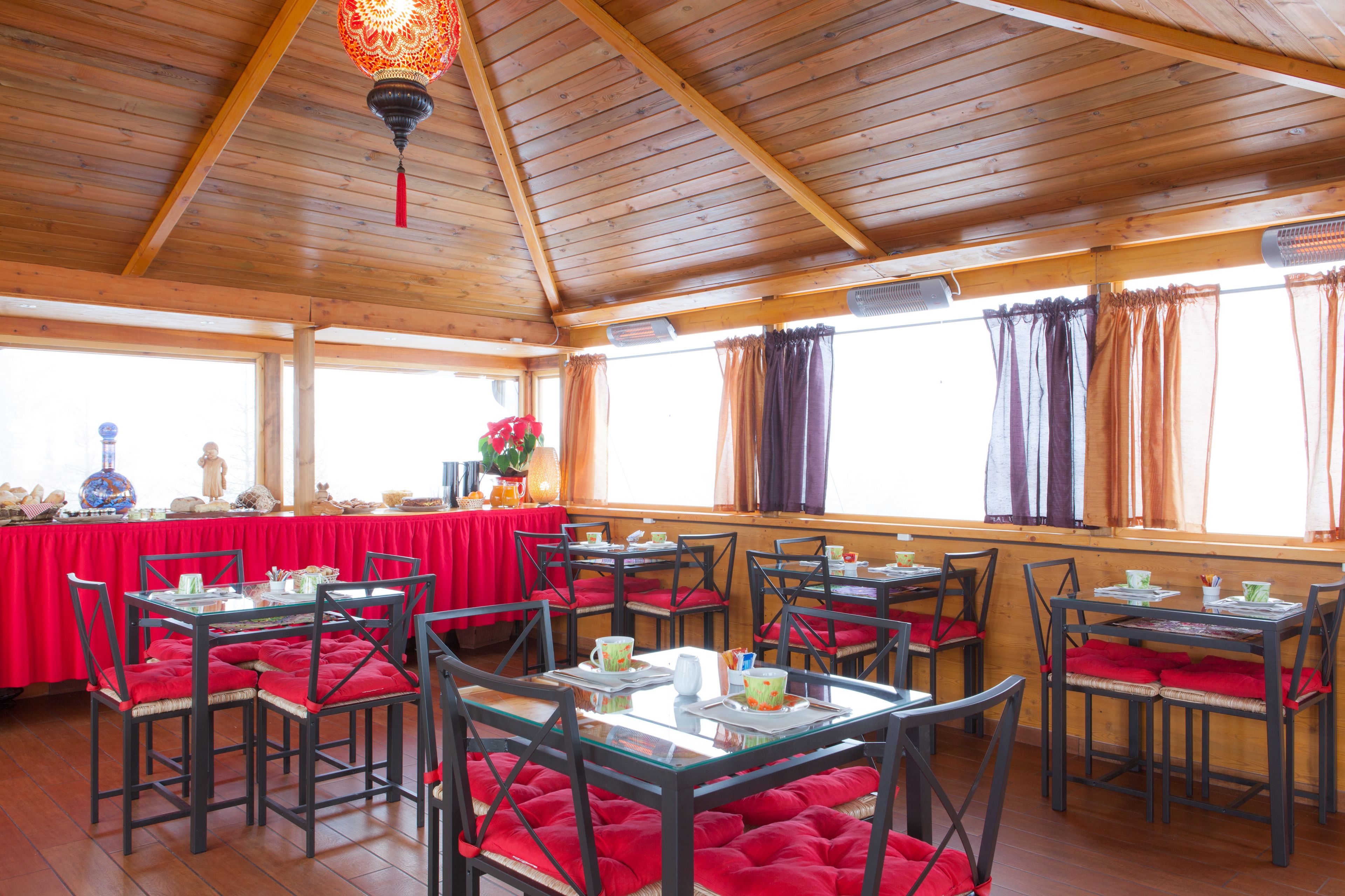 A restaurant with wooden ceiling beams, red cushioned chairs, and tables set for dining.