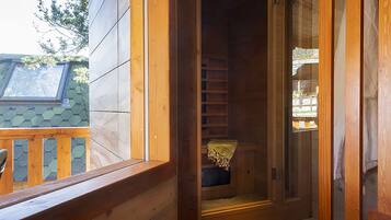 Une cabane en bois avec une porte en verre donnant sur une petite salle de bain fermée, équipée d’un banc et d’une serviette accrochée au mur.