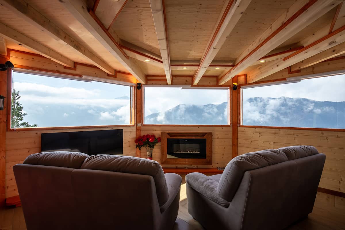 Acogedora habitación con dos sofás frente a una chimenea y amplias ventanas con vistas a la montaña.
