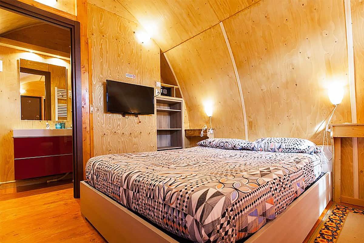 Un dormitorio acogedor con techo inclinado, cama con ropa de cama estampada, televisor montado en la pared y cómoda de madera.