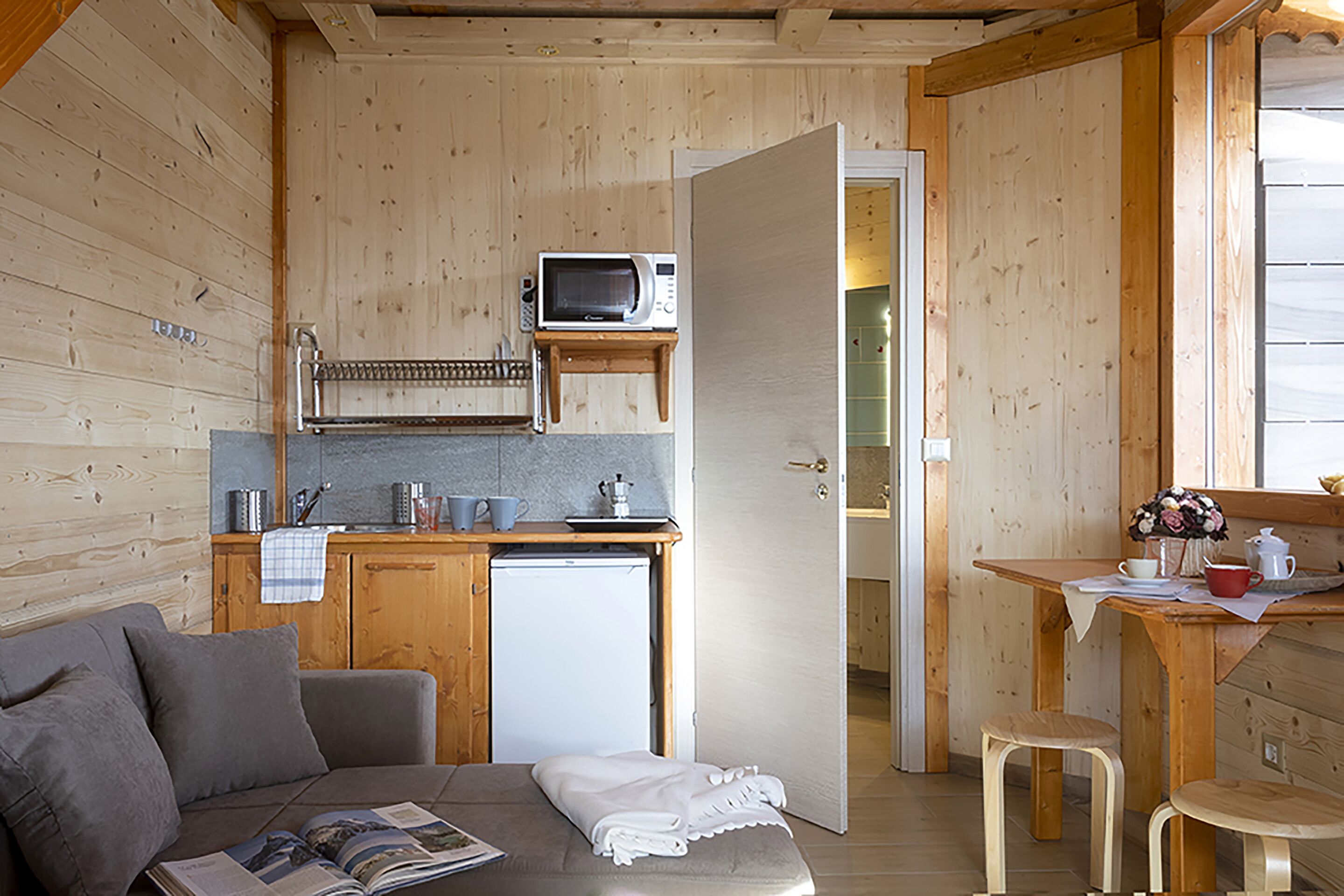 A compact, wood-paneled room with a kitchenette, a small refrigerator, a microwave, and a dining area with stools.