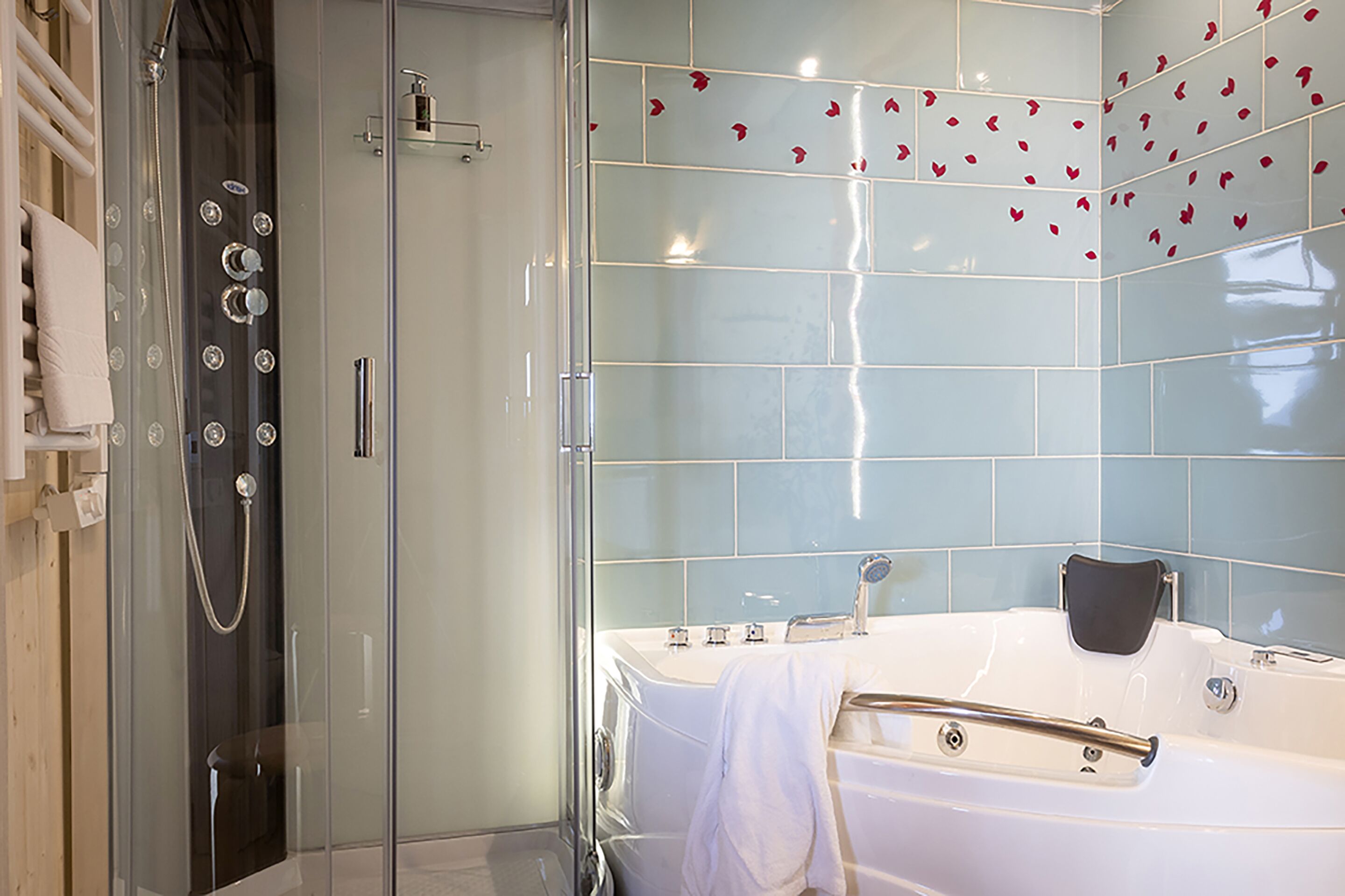 A modern bathroom with a glass-enclosed shower, a freestanding bathtub, and a tiled wall with red flower decals.