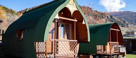 Two green, A-frame cabins with wooden balconies and a stone pathway leading to them.