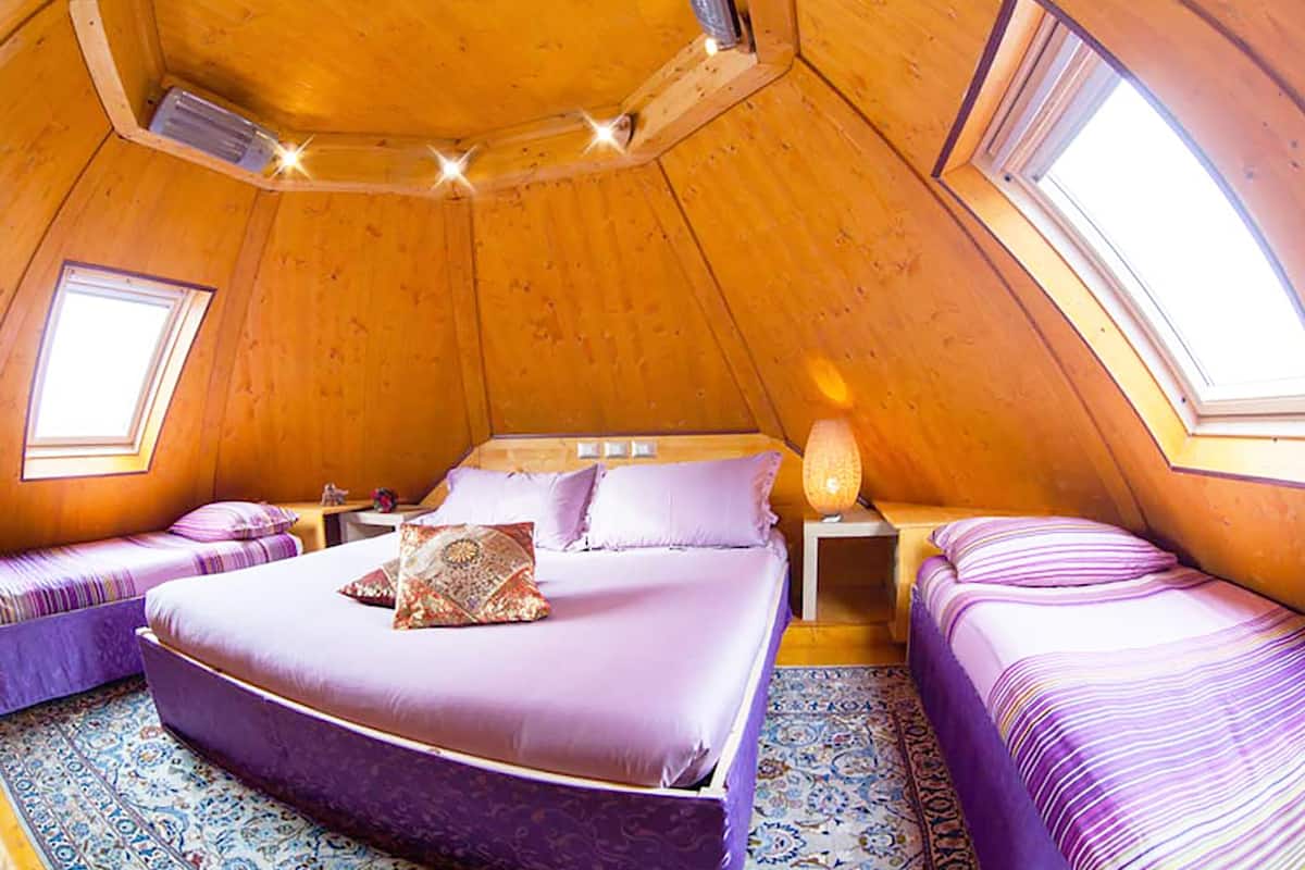 Un dormitorio acogedor de forma triangular con una cama grande, dos camas más pequeñas y un tragaluz.