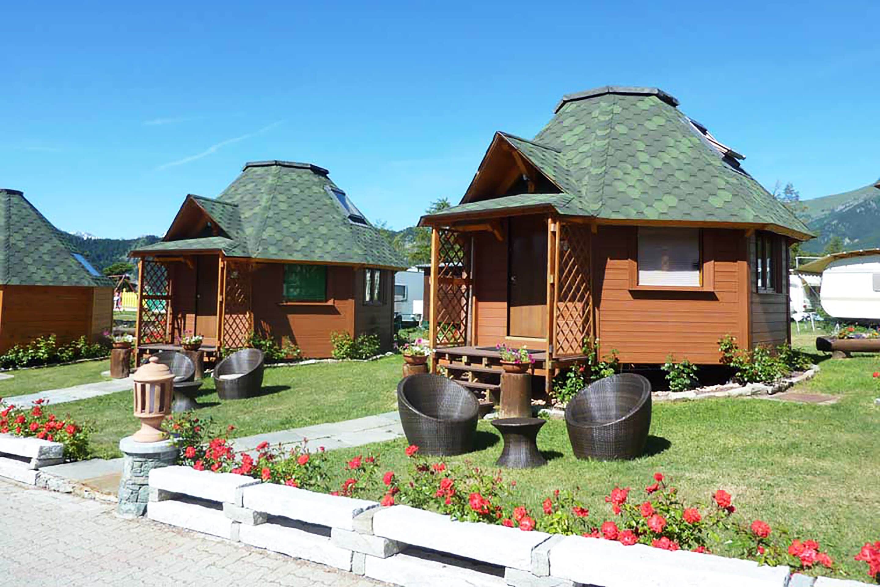 Eine Reihe von Holzhütten mit geneigten Dächern, jede mit einer Veranda und Sitzgelegenheiten im Freien.