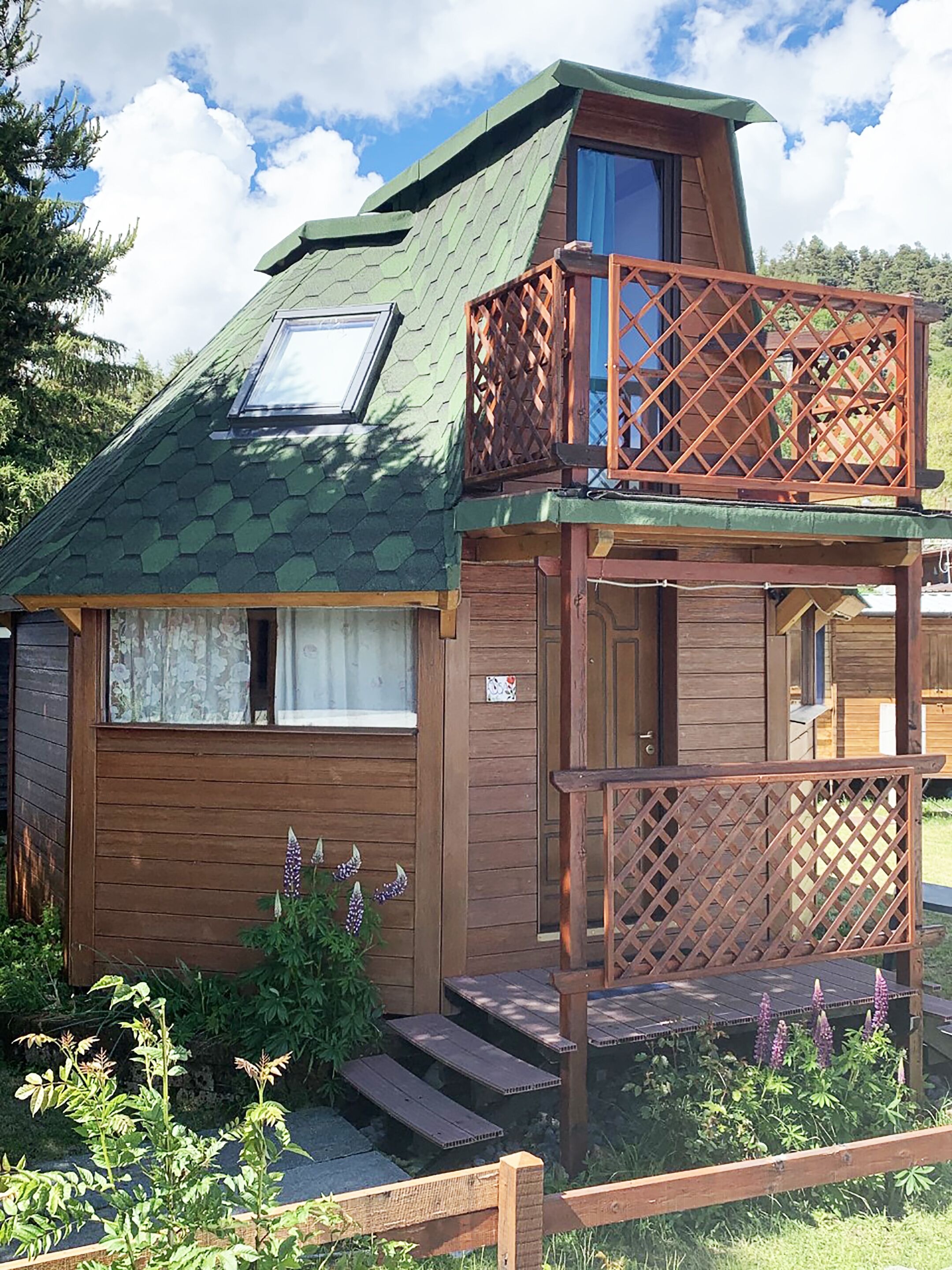 A cabin with a green roof, a wooden deck, and a small balcony.