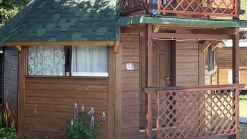 A cabin with a green roof, a wooden deck, and a small balcony.