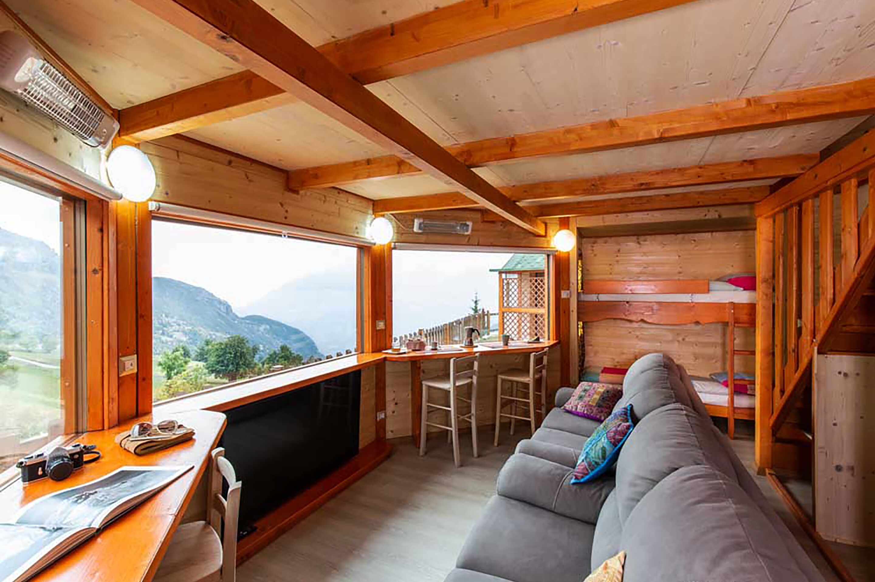 A cozy cabin interior with a wooden ceiling, a sofa, a dining area, and a view of mountains.