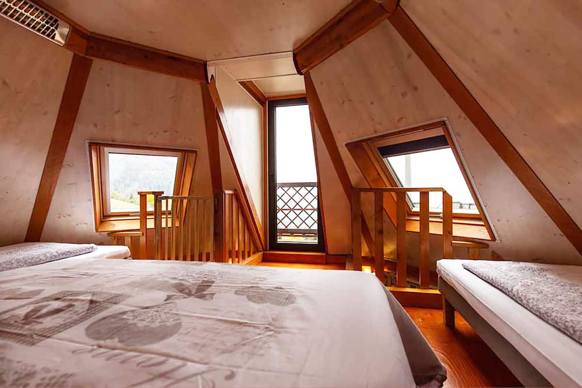 Una habitación con dos camas, vigas de madera y un balcón con puerta ajuada.