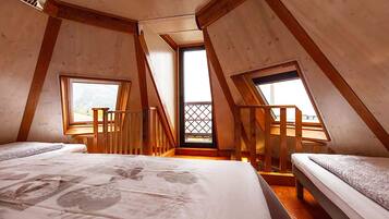 A room with two beds, wooden beams, and a balcony with a lattice door.