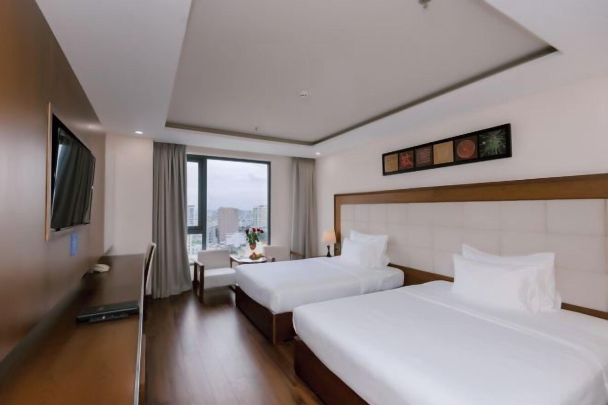 Une chambre d’hôtel avec deux lits, un bureau, une chaise, une télévision et une fenêtre donnant sur la ville.