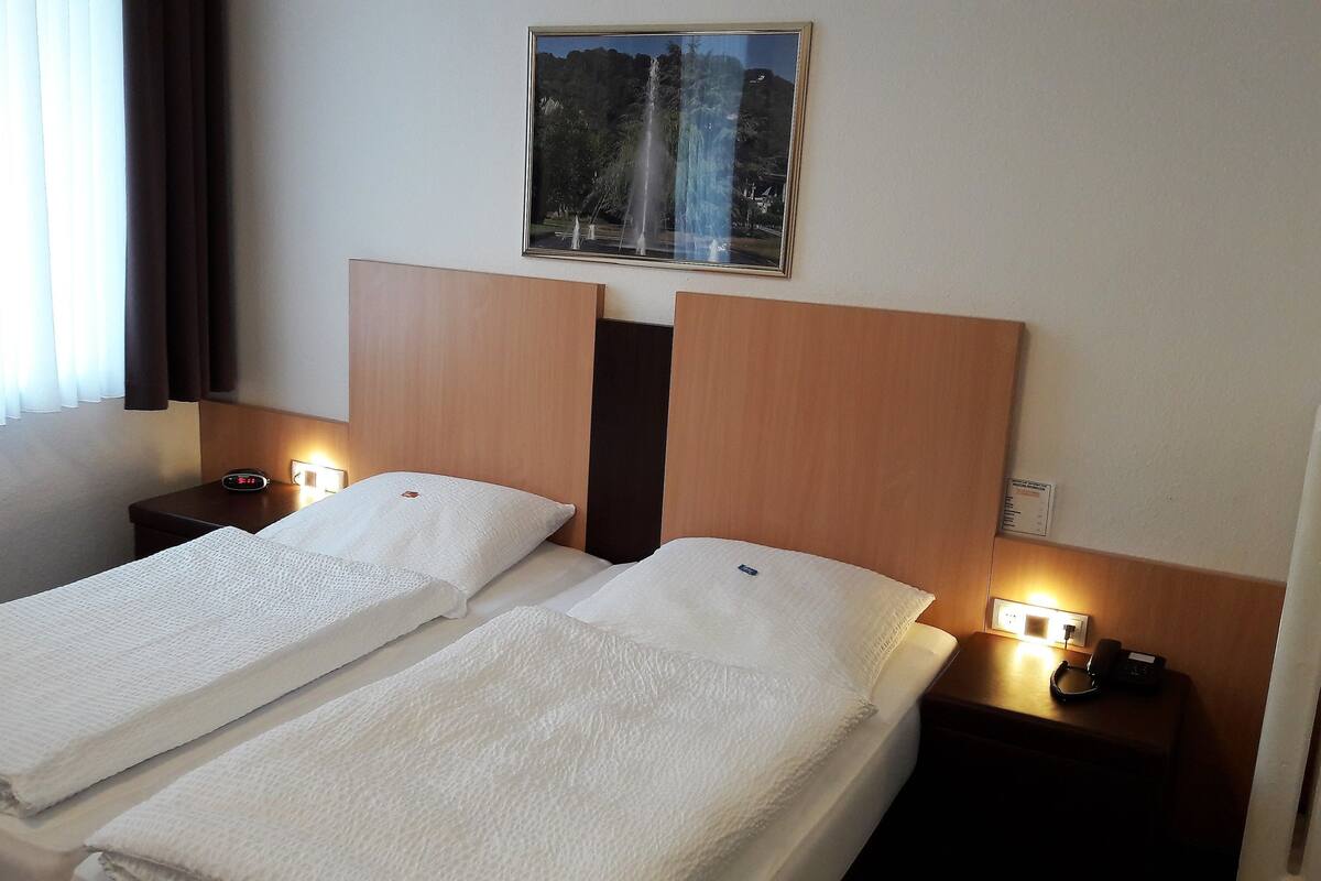 A hotel room with two beds, a painting above the beds, and bedside lamps.