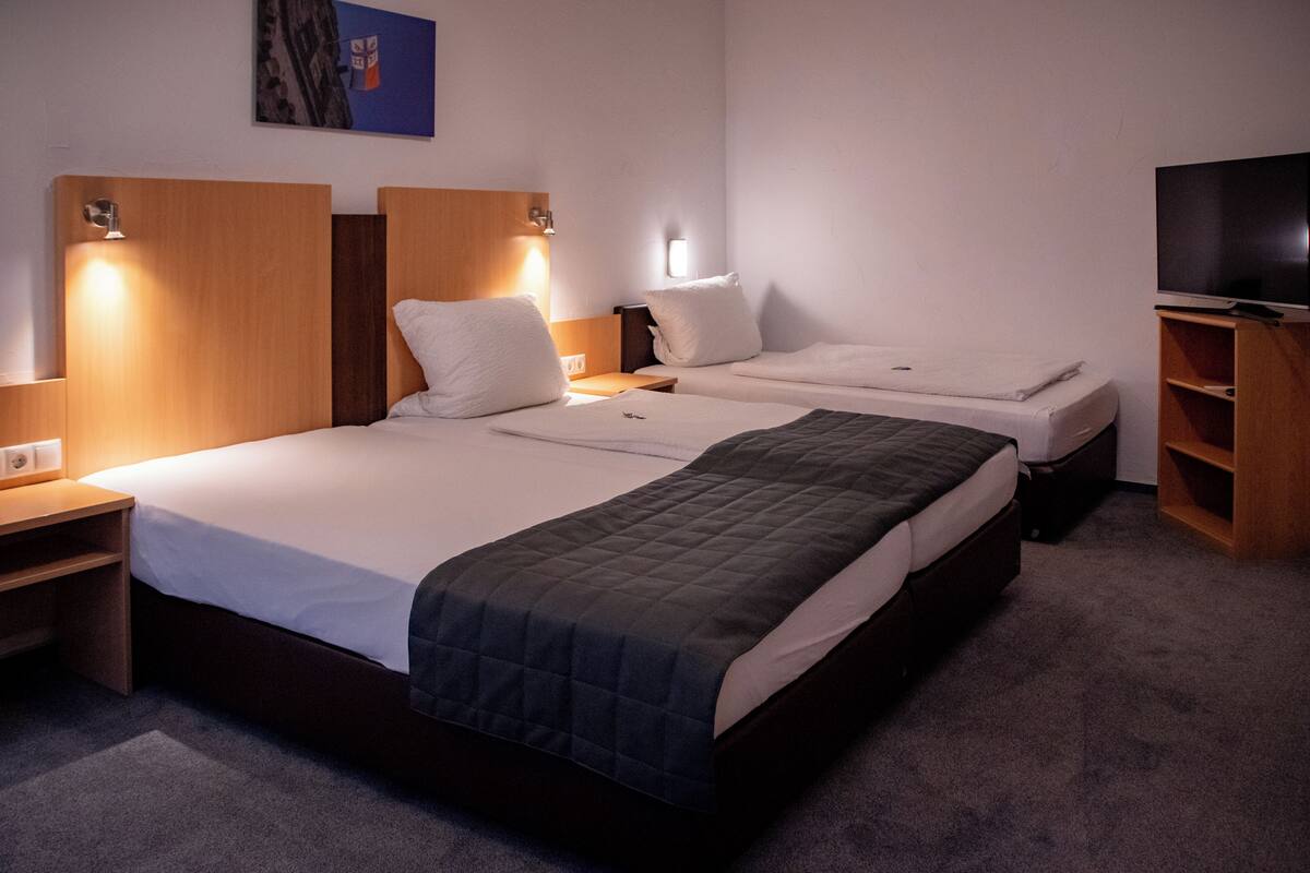 A hotel room with two beds, a TV, and a painting on the wall.