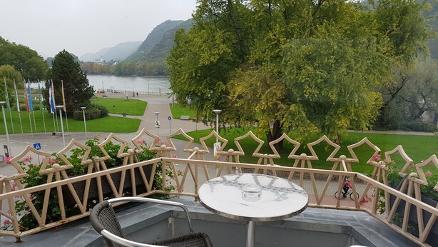 Ein Sitzbereich im Freien mit Tisch und Stühlen mit Blick auf einen See und viel Grün.
