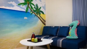 Habitación con un mural de playa, un sofá con un cojín con forma de dinosaurio y una mesita con una bandeja de objetos.