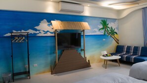 Una habitación con un mural de playa, una cama individual, una mesita pequeña y un sofá.