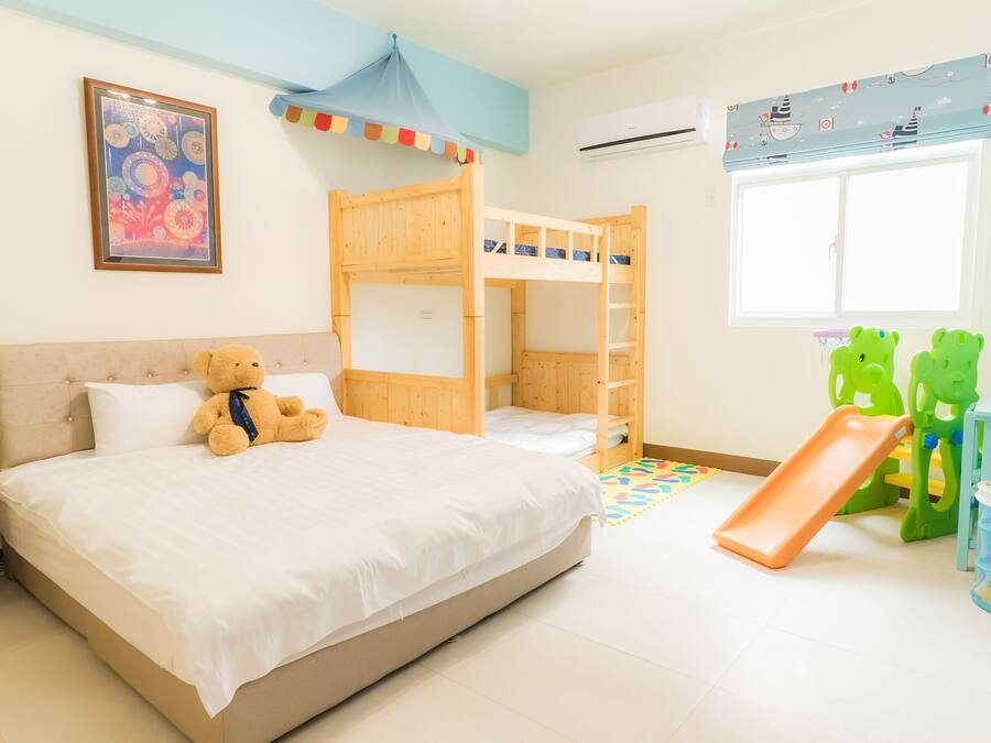 A child's bedroom with bunk beds, a teddy bear, a slide, and a green toy structure.