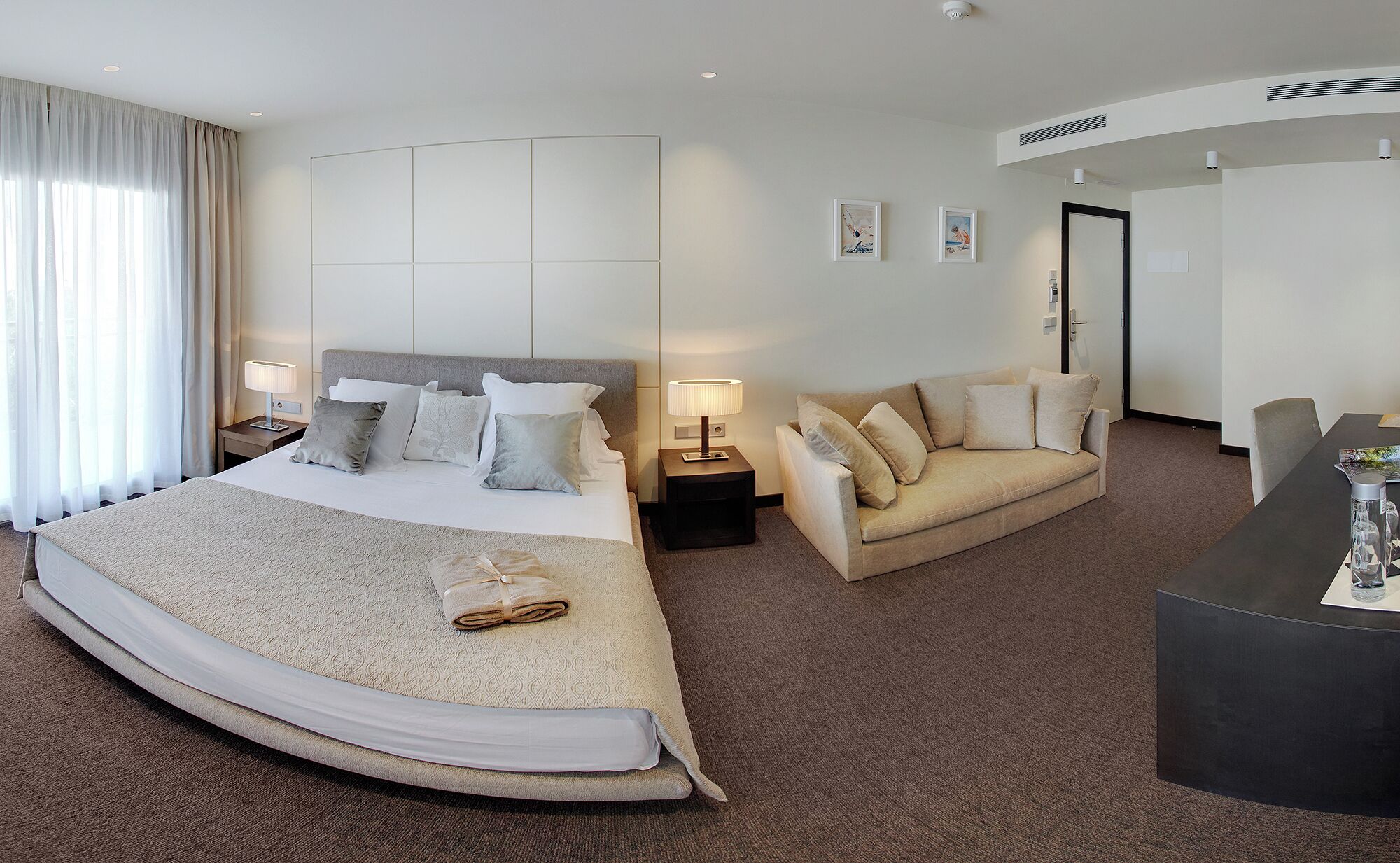 A hotel room with a large bed, a sofa, a desk, and a door.