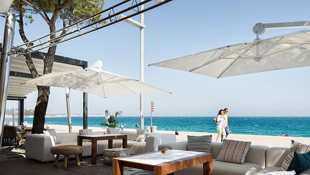 Een terras met witte meubels en parasols, met uitzicht op zee.