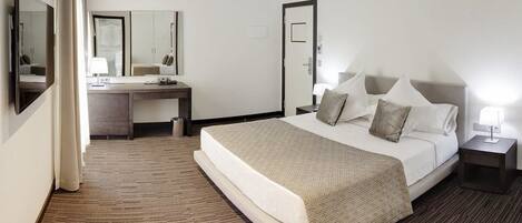 A hotel room with a bed, a desk, a chair, a mirror, and a nightstand.