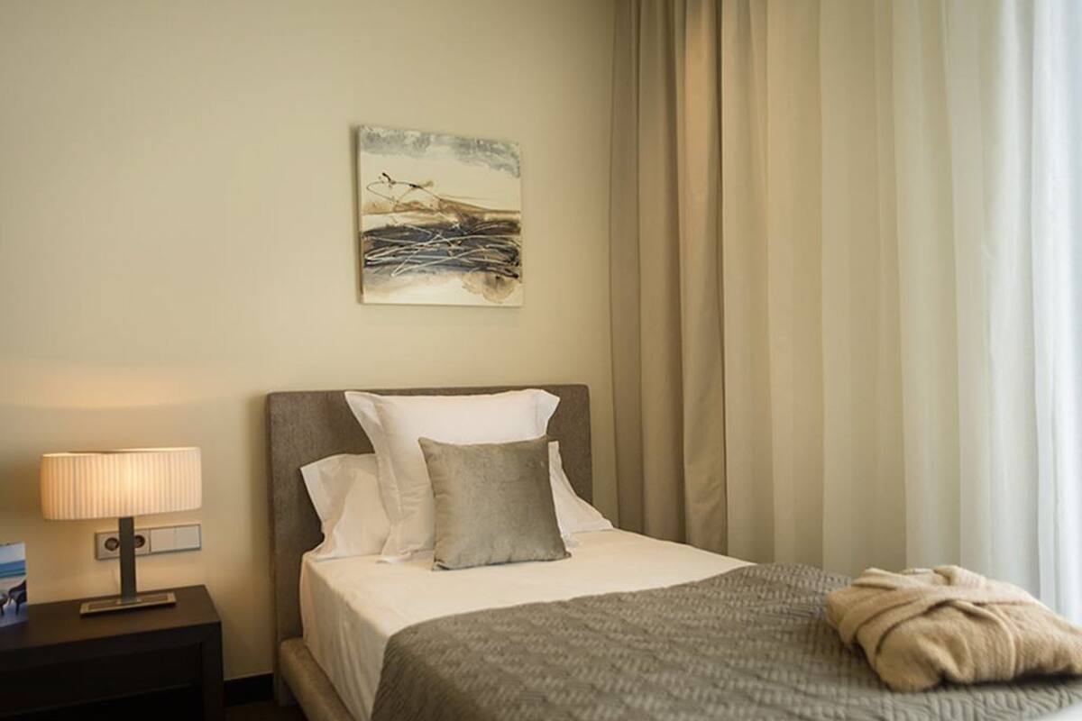 Een hotelkamer met een bed, een nachtkastje met lamp, een schilderij aan de muur, en een raam met gordijnen.
