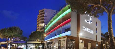 A modern hotel with a multi-story structure, outdoor seating area, and a well-lit entrance.