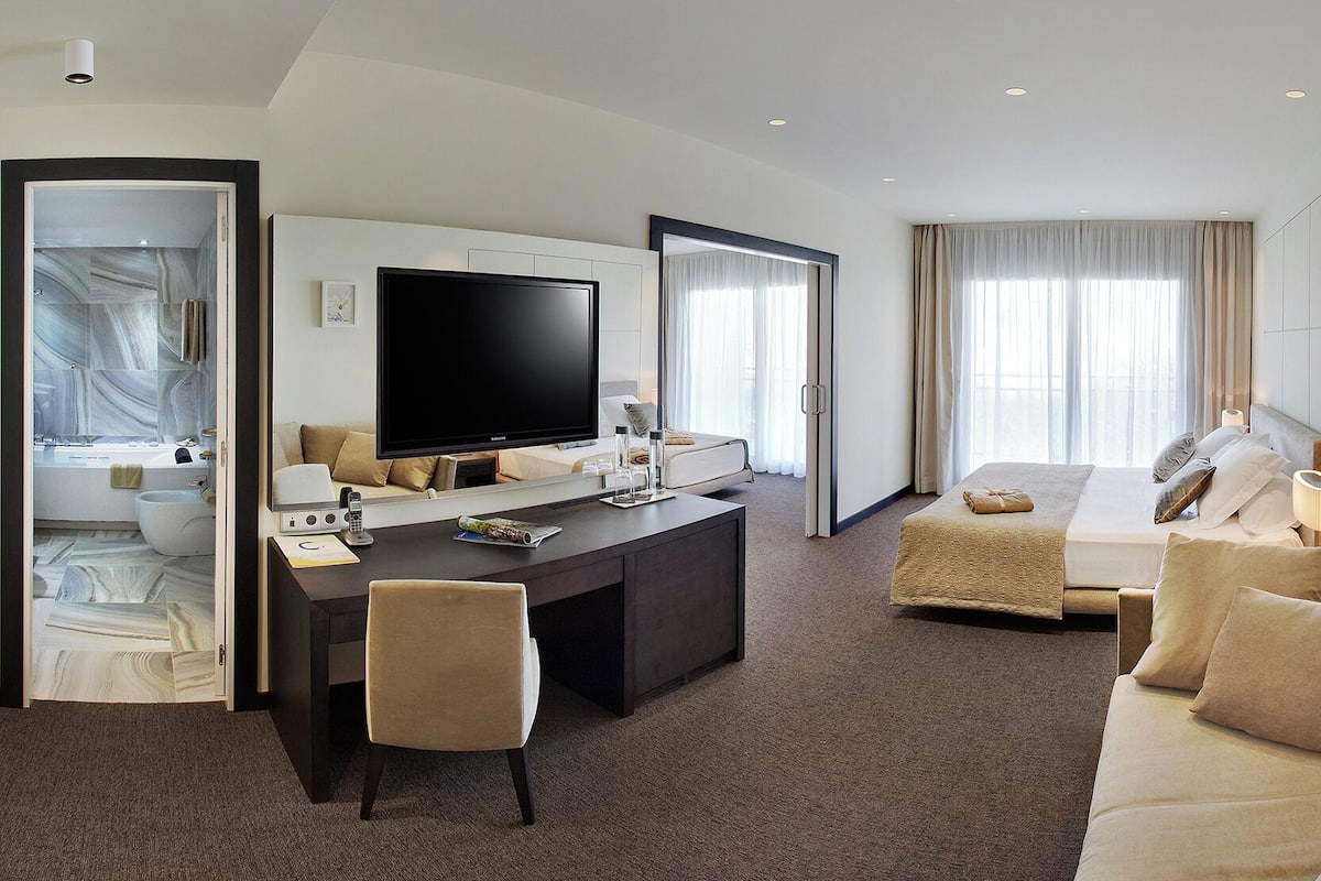 Een hotelkamer met een grote flatscreen-tv, een bureau met stoel, een bed met hoofdeinde en een grote spiegel.