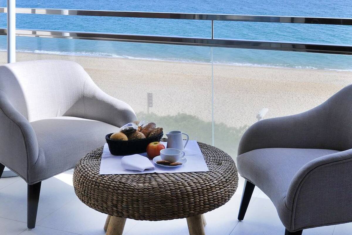 Een balkon met twee stoelen, een rieten tafel met een fruitmand, een beker en een bord.