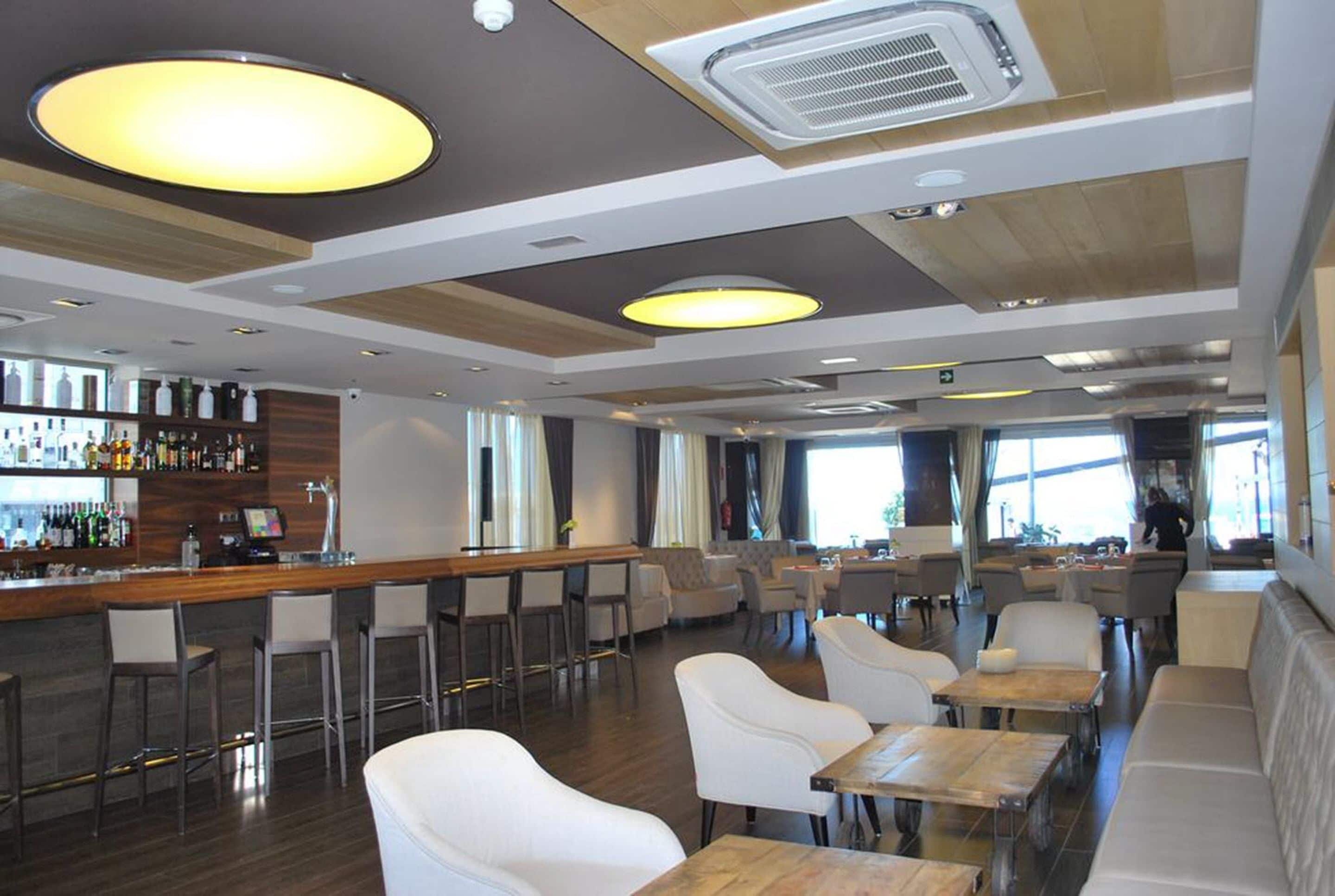 A modern bar area with a wooden counter, bar stools, and a seating area with white chairs and tables.