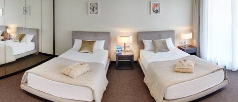 Habitación de hotel con dos camas, un espejo grande y una mesita de noche con lámpara.