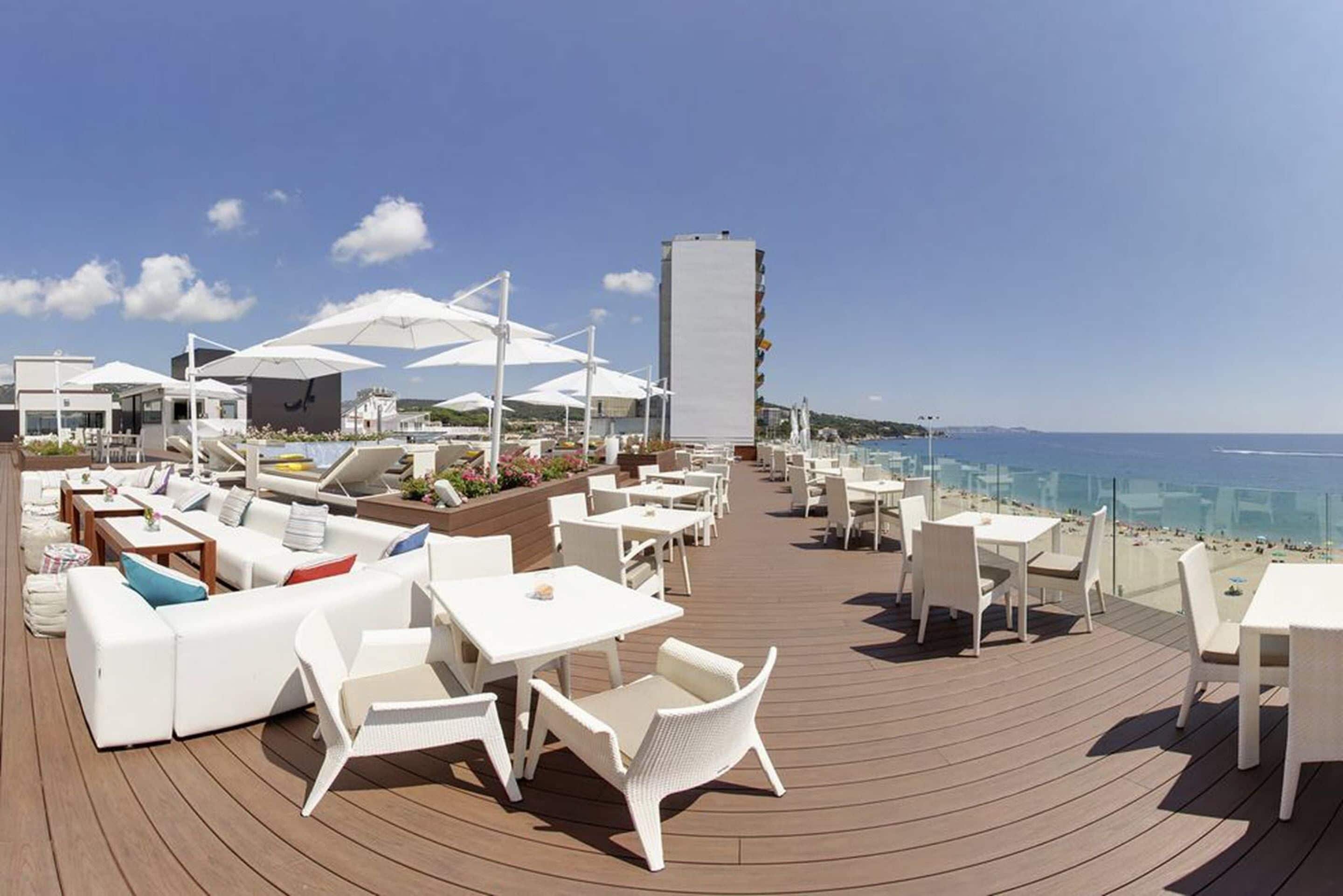 Eine Dachterrasse mit weißen Möbeln, Sonnenschirmen und Meerblick.