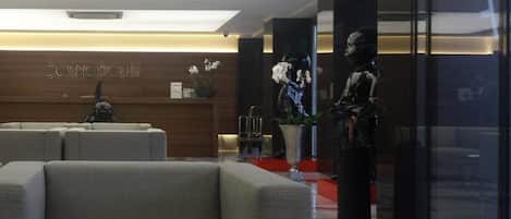 Un área de recepción moderna con mostrador, zona de estar y esculturas decorativas.