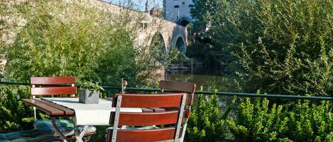An outdoor seating area with a table and chairs, overlooking a river and a historic building.