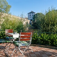 Un área de estar al aire libre con una mesa y sillas, con vista a un río y un edificio histórico.