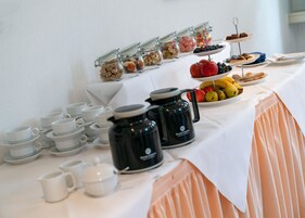 Una mesa de buffet con diferentes opciones de comida, como frutas, frutos secos y pasteles, además de varias cafeteras y tazas de té.