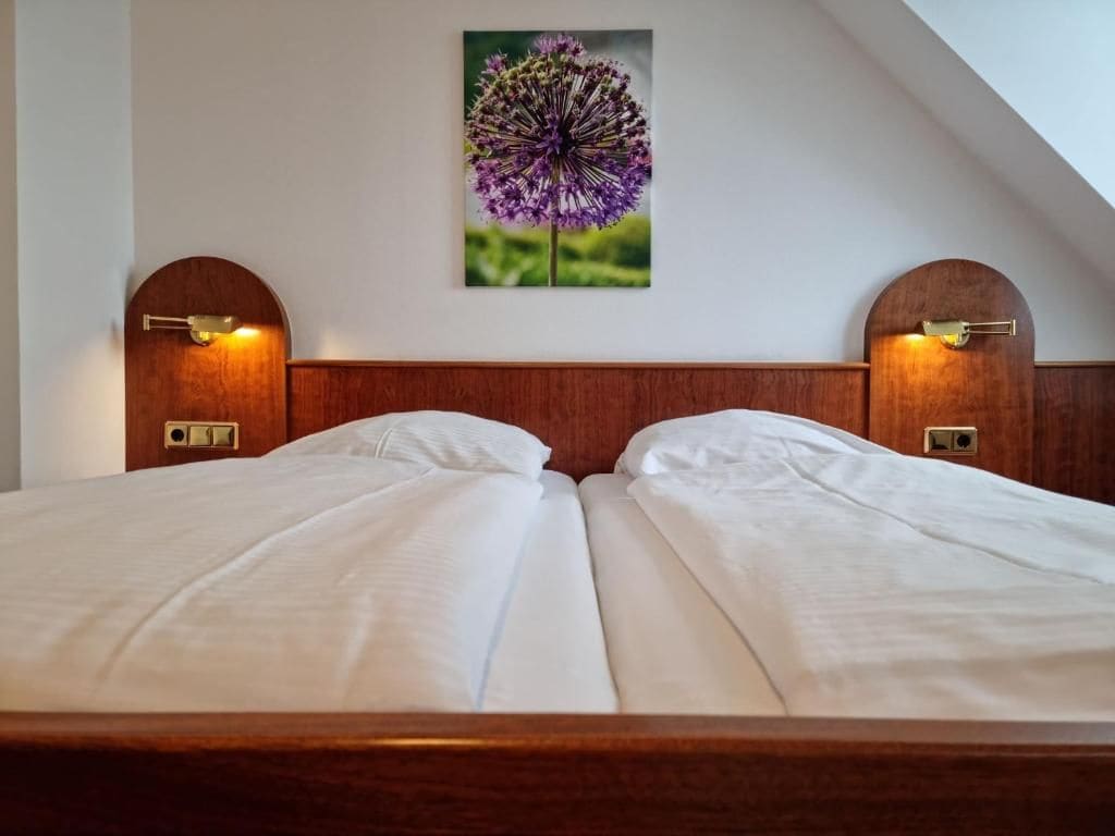 A double bed with a wooden headboard, two wall-mounted lamps, and a framed floral artwork above it.