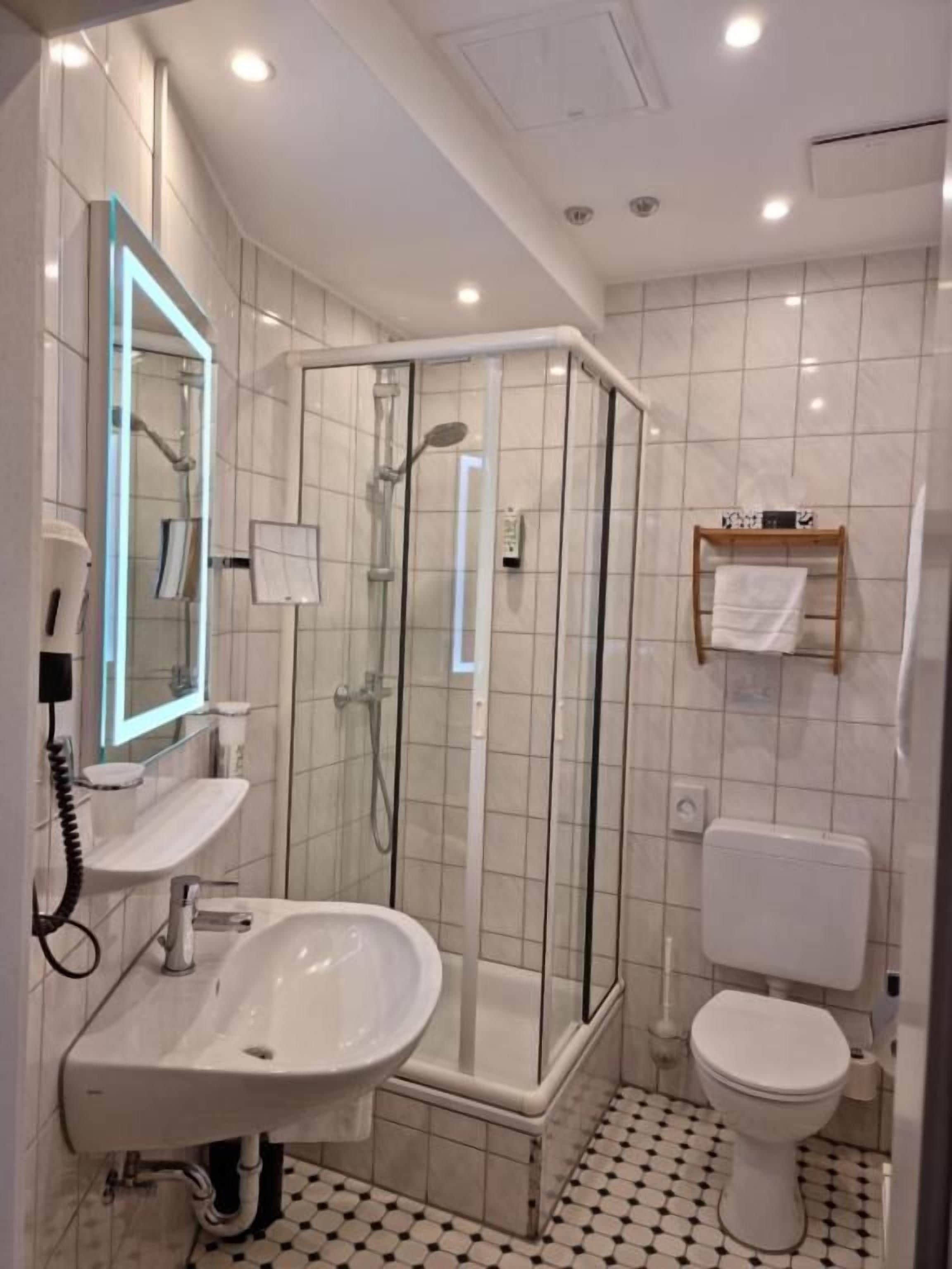 Un baño con ducha de mampara de vidrio, lavamanos e inodoro.