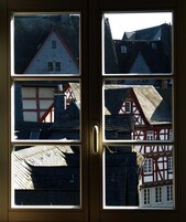 Una puerta con vistas a arquitectura europea tradicional, incluyendo una casa de entramado madera rojo y blanco y una casa gris con tejado rojo.