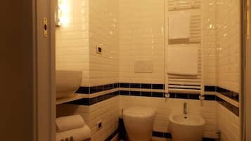 Une salle de bain avec des carreaux de céramique blancs rectangulaires, un lavabo blanc, des toilettes et un bidet.