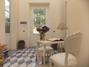 A room with a checkered floor, a white table with a vase of flowers, a chair, and a lamp. - B&B Di Camilla (Pisa)