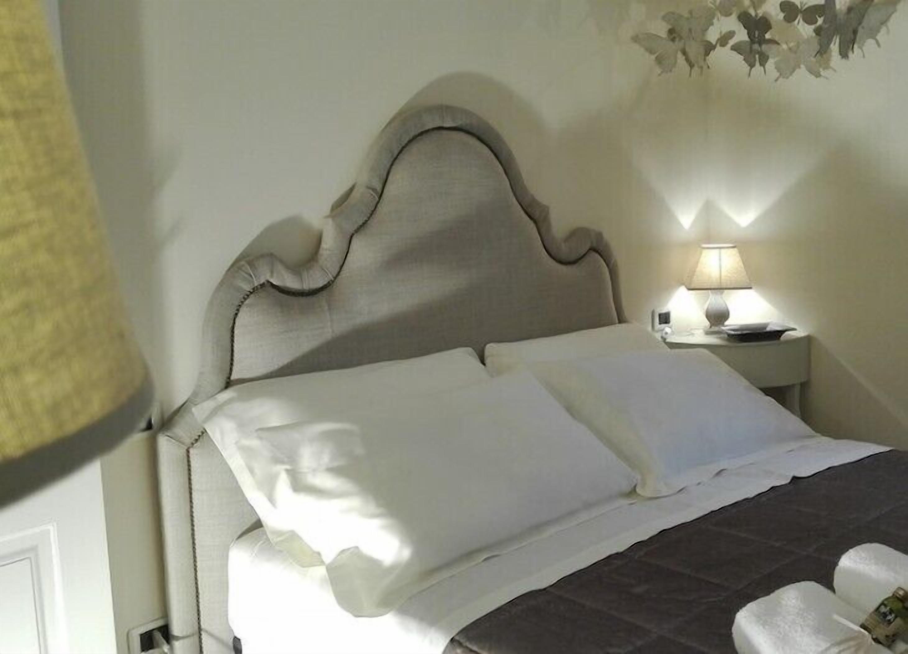 A neatly made bed with white linens and a dark bedspread, a bedside lamp, and a wall with a floral pattern.