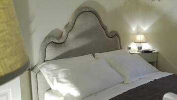 A neatly made bed with white linens and a dark bedspread, a bedside lamp, and a wall with a floral pattern.